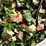 Chopped Kale Salad in round white bowl with black utensils scooping some up.