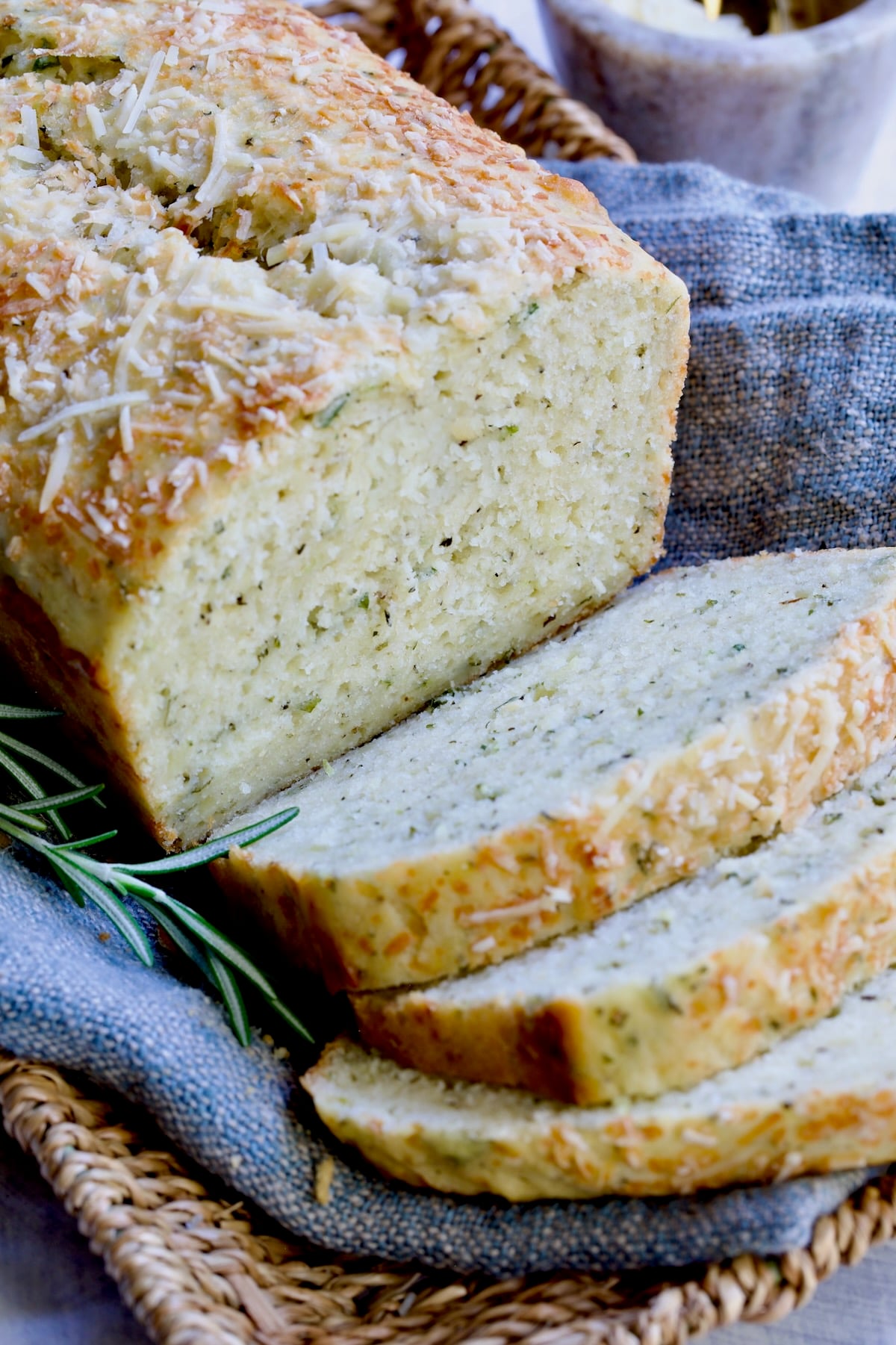 Sliced loaf of Easy Herb Bread on blue napkin in wicker basket.