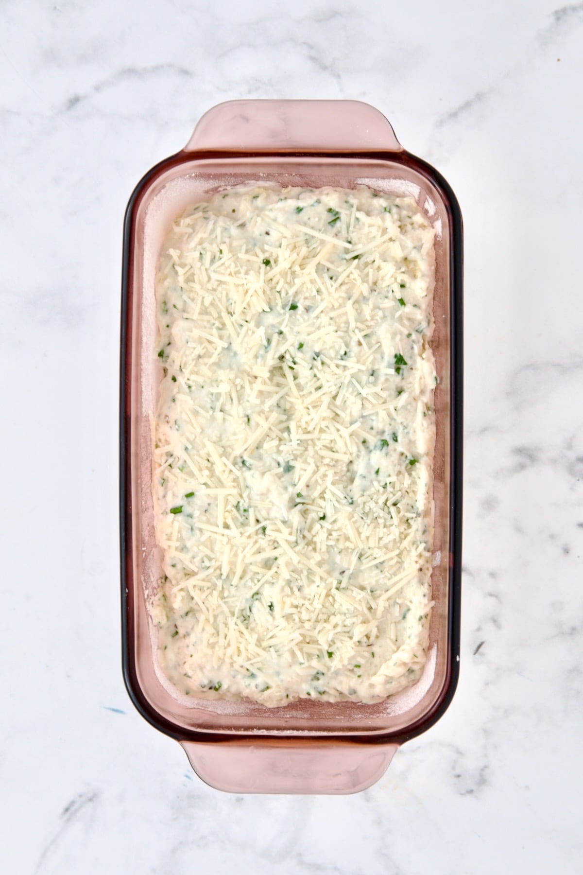 Unbaked herb bread in glass baking dish.