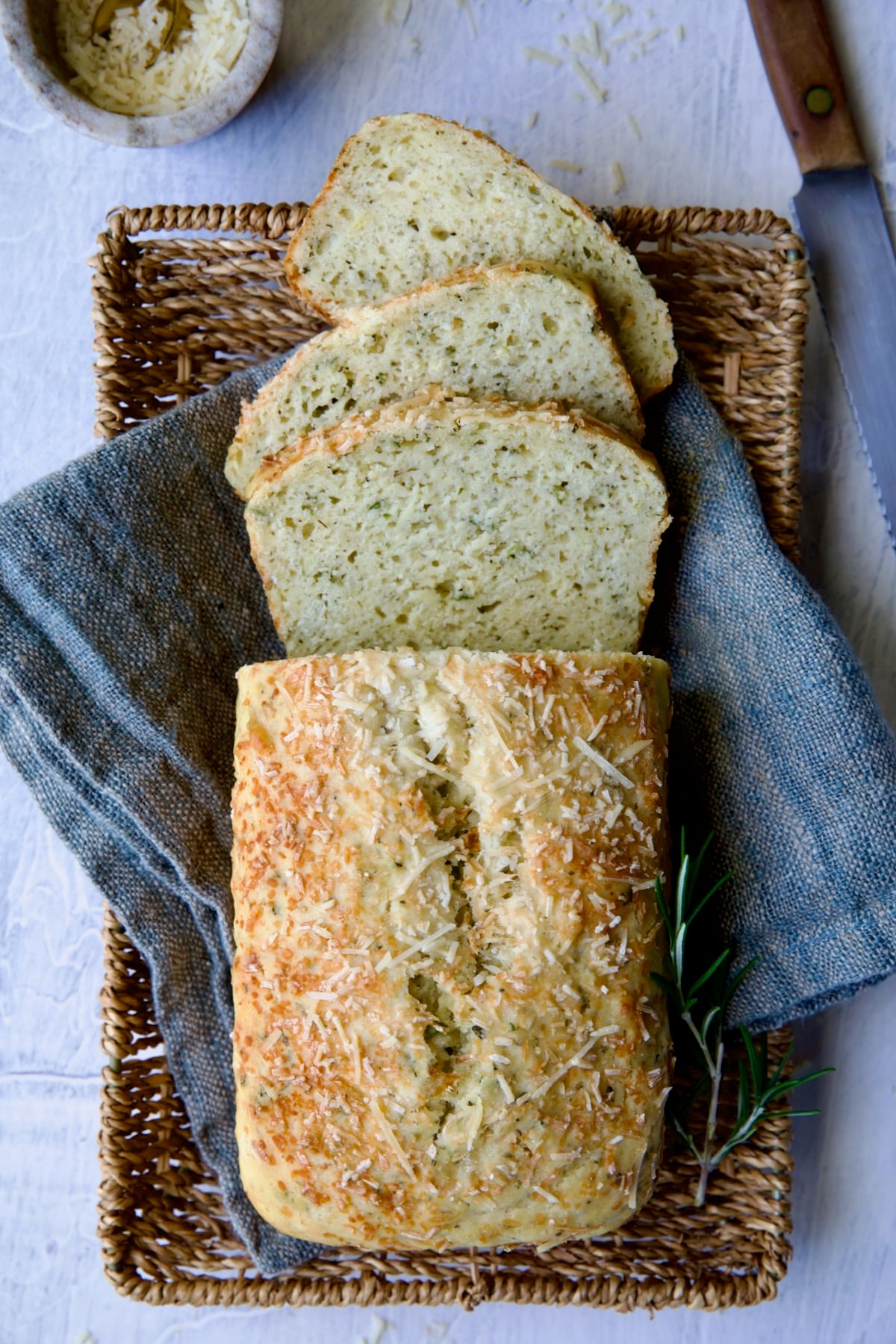 Sliced loaf of Easy Herb Bread on blue napkin in wicker basket.