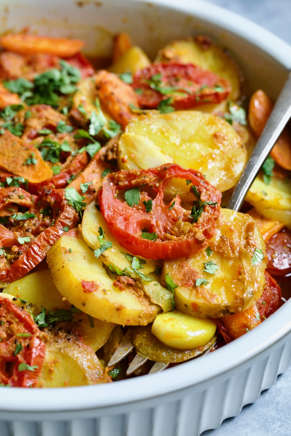 Moroccan Potato Tagine in round white baking dish with serving fork lifting some out.