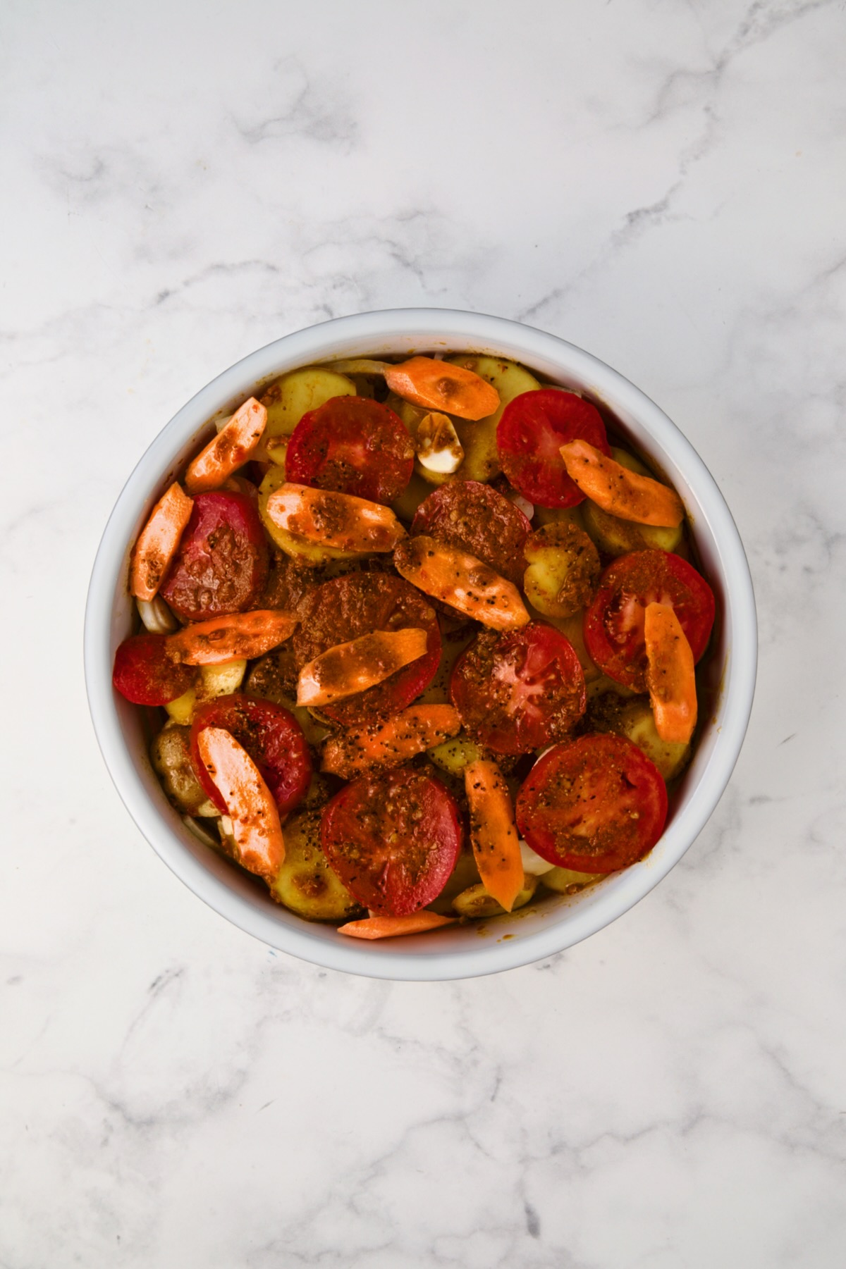 Assembled tagine before being baked in round white baking dish.