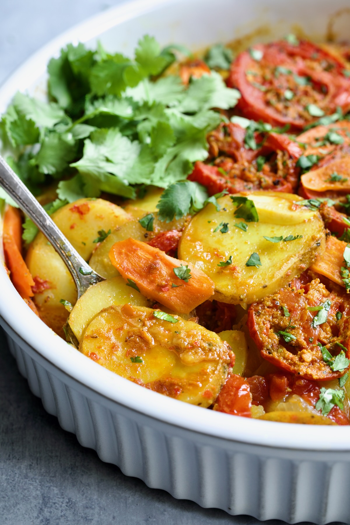 Moroccan Potato Tagine in round white baking dish with serving fork lifting some out.