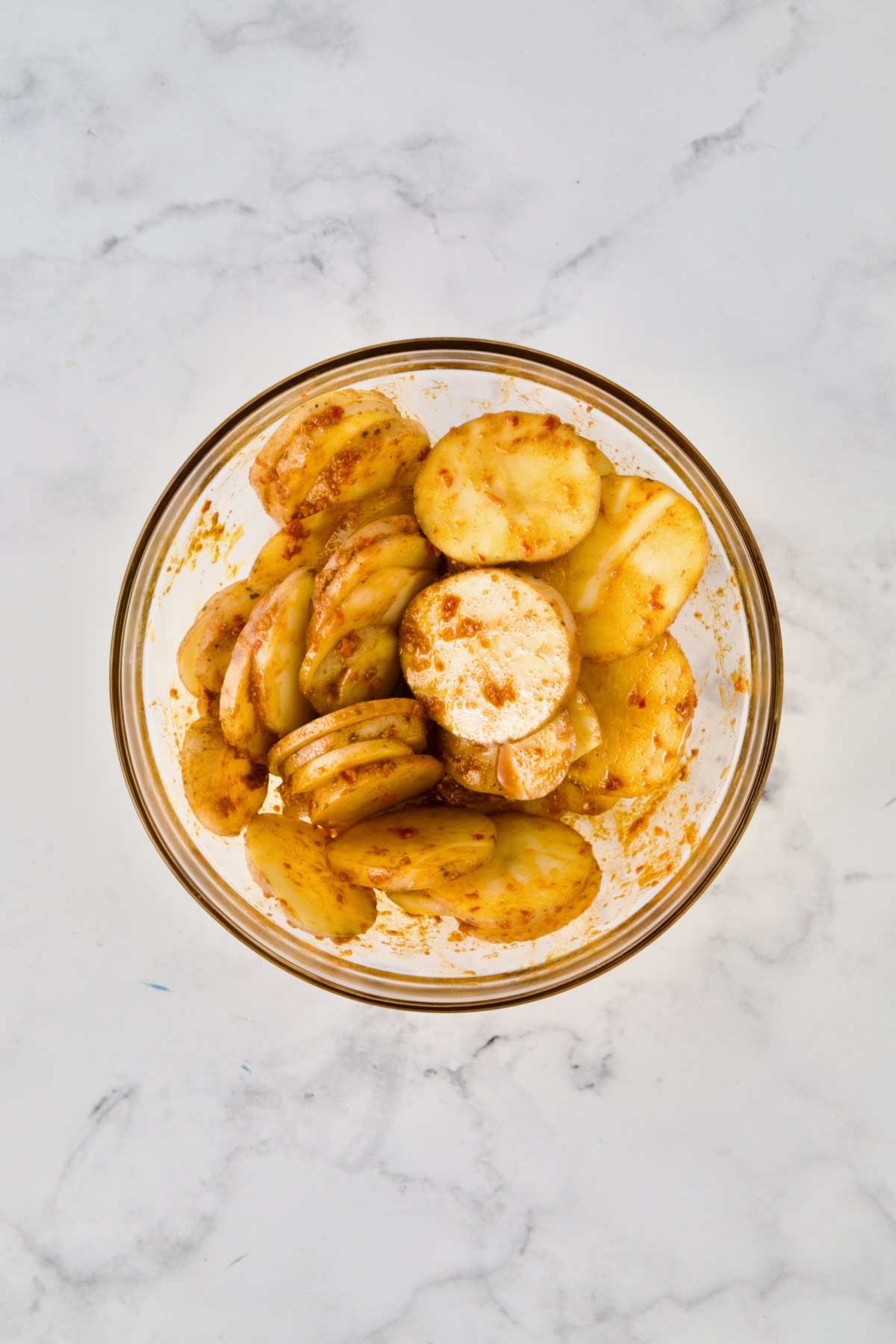 Potatoes tossed with spice and oil combination in glass bowl.