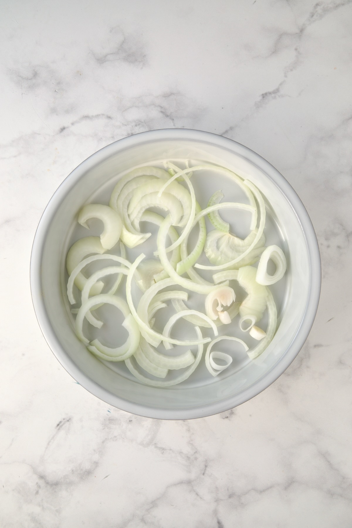 Sliced onions in the bottom of a round white baking dish.