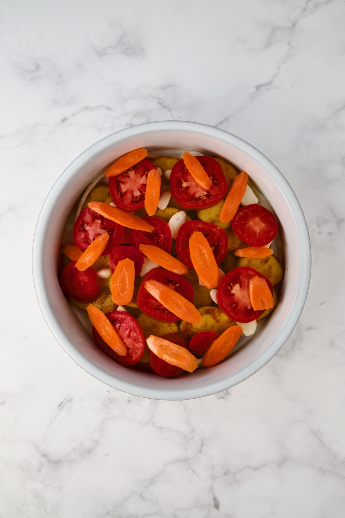 Carrots placed over tomatoes in round white baking dish.