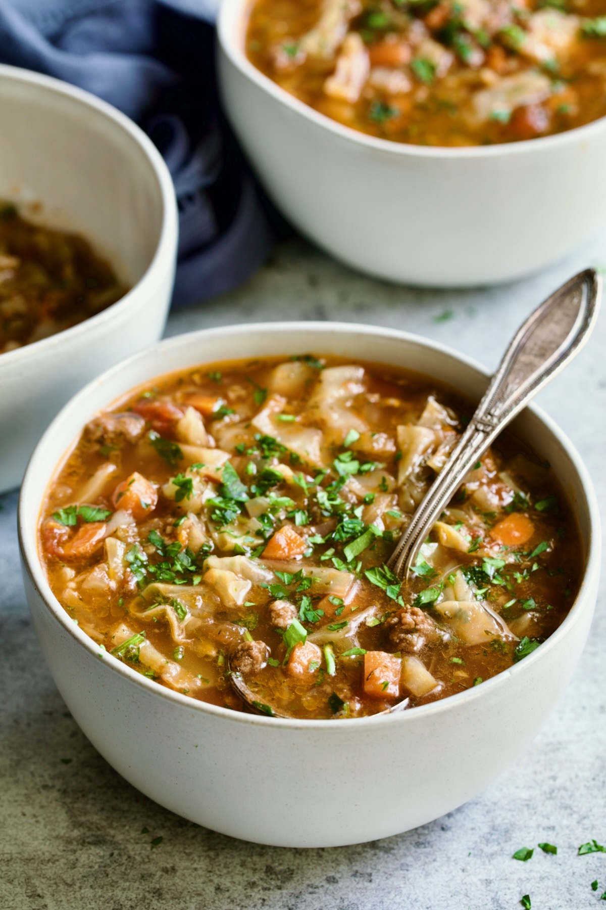 Three servings of Beef and Cabbage Soup each in a white soup bowl.