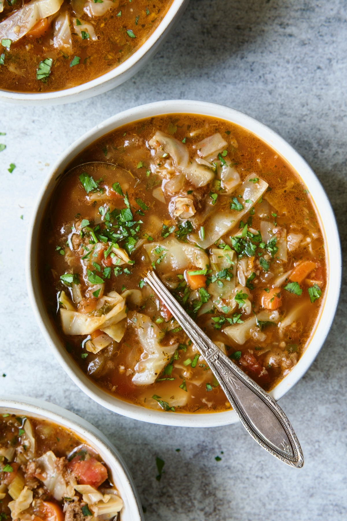 One serving of Beef and Cabbage Soup in white soup bowl with soup spoon.