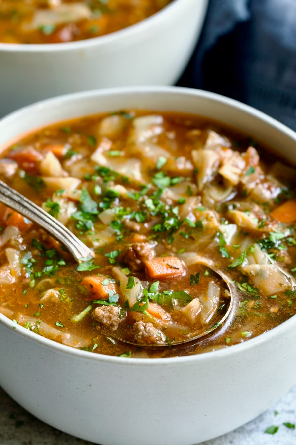 One serving of Beef and Cabbage Soup in white soup bowl with soup spoon.