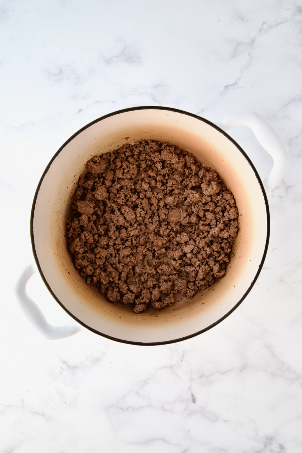 Cooked ground beef in white Dutch oven.