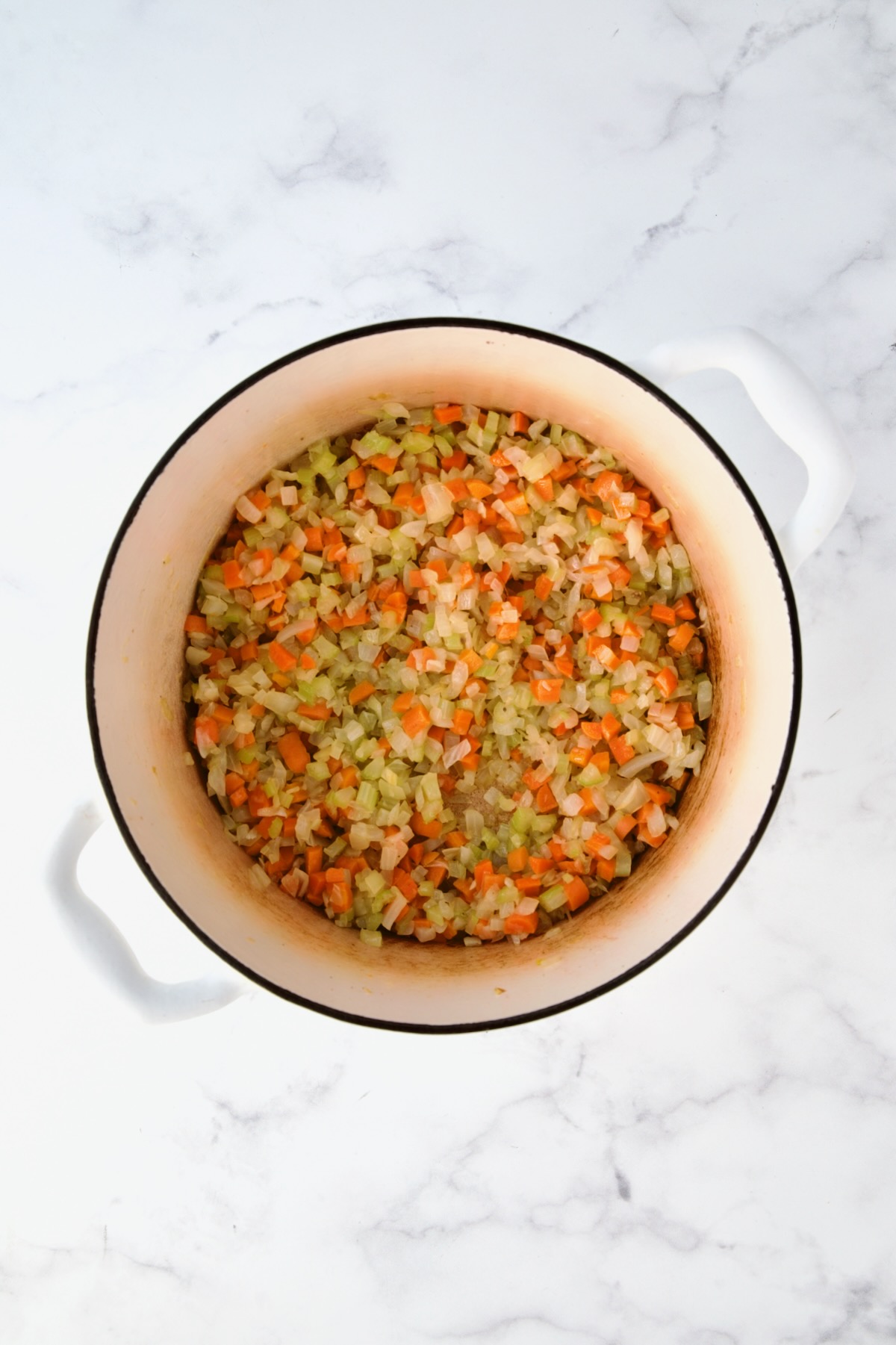 Cooked onions, carrots and celery in white Dutch oven.