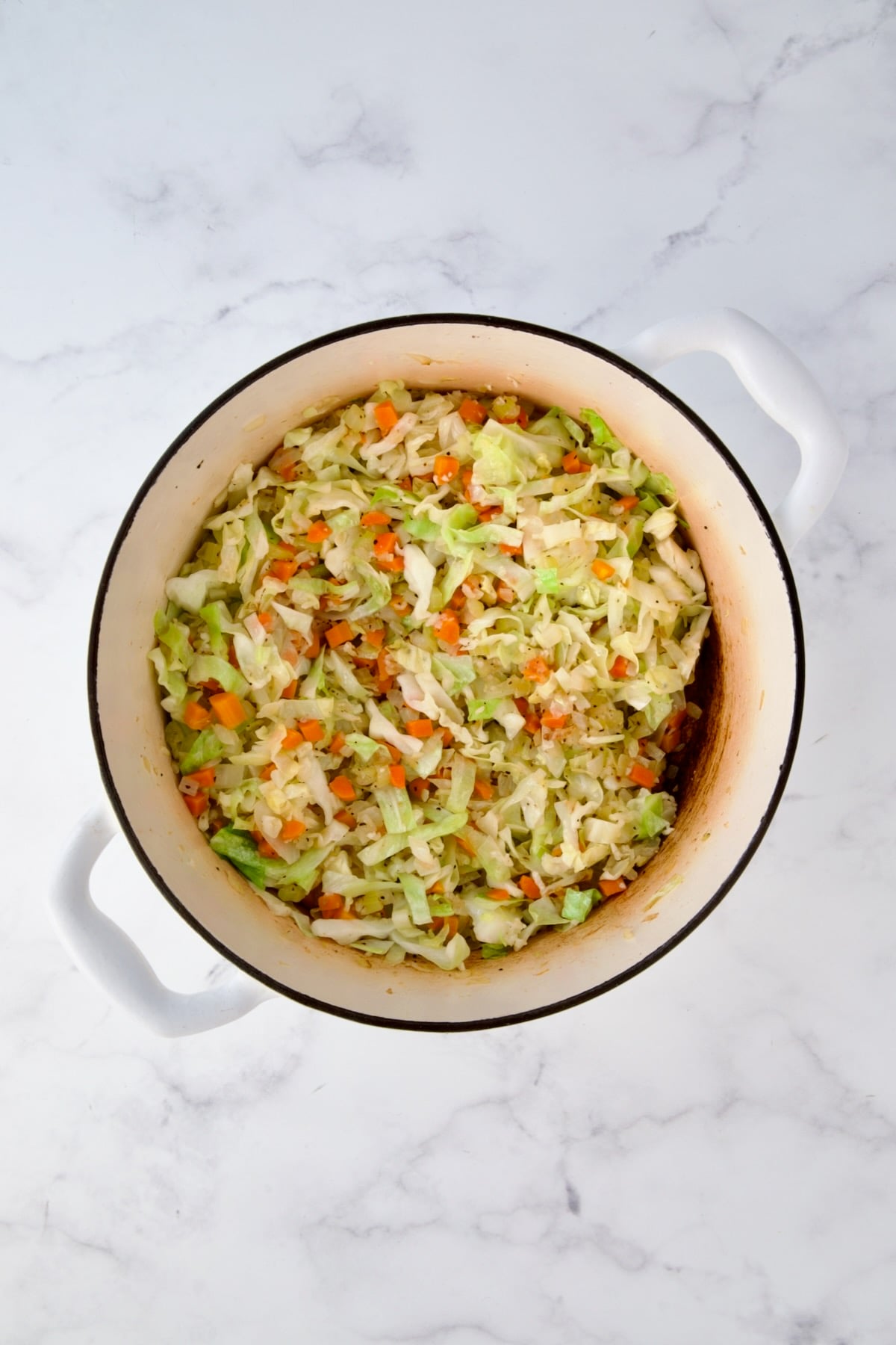 Cooked onions, carrots, celery and cabbage in white Dutch oven.