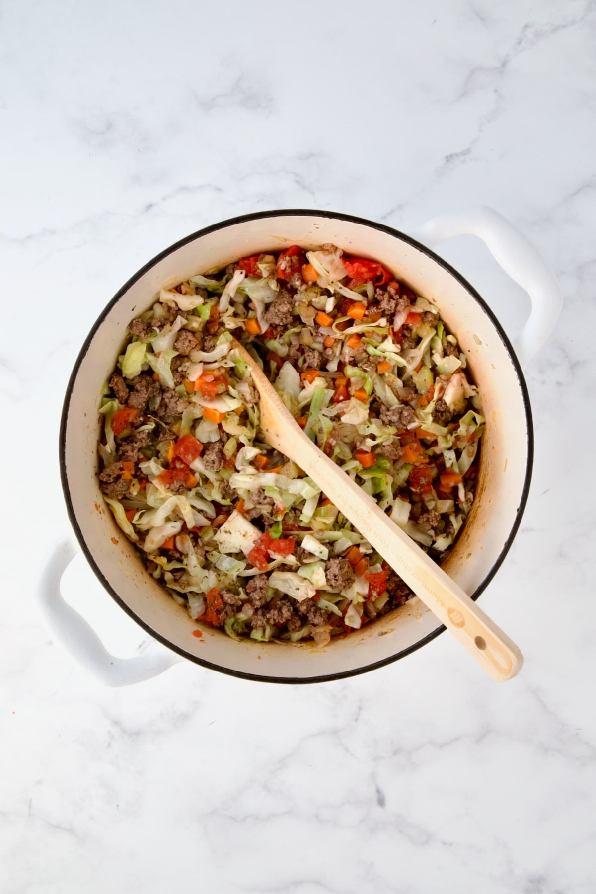 Cooked ground beef added to onions, carrots, celery and cabbage in white Dutch oven.