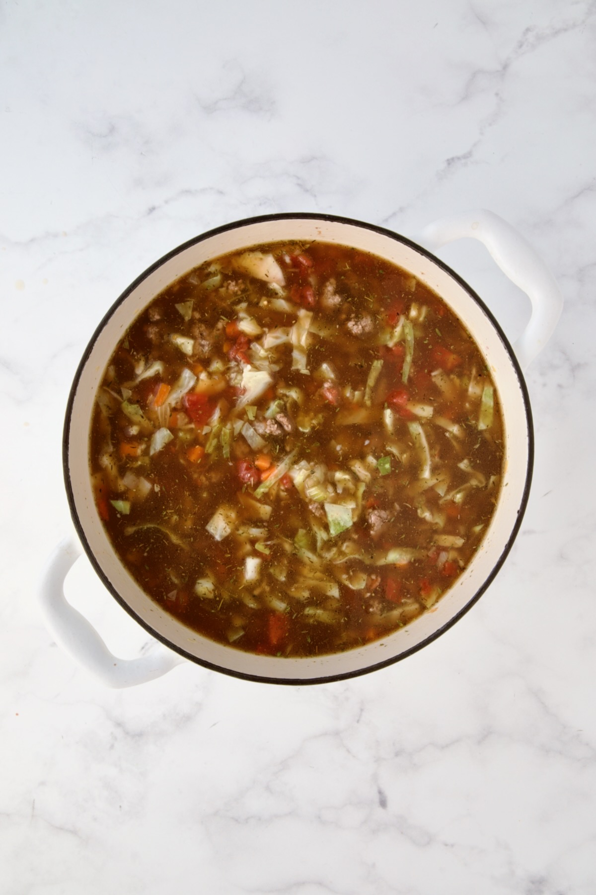 Beef broth, diced tomatoes, tomato sauce and herbs added to vegetables and beef in white Dutch oven.