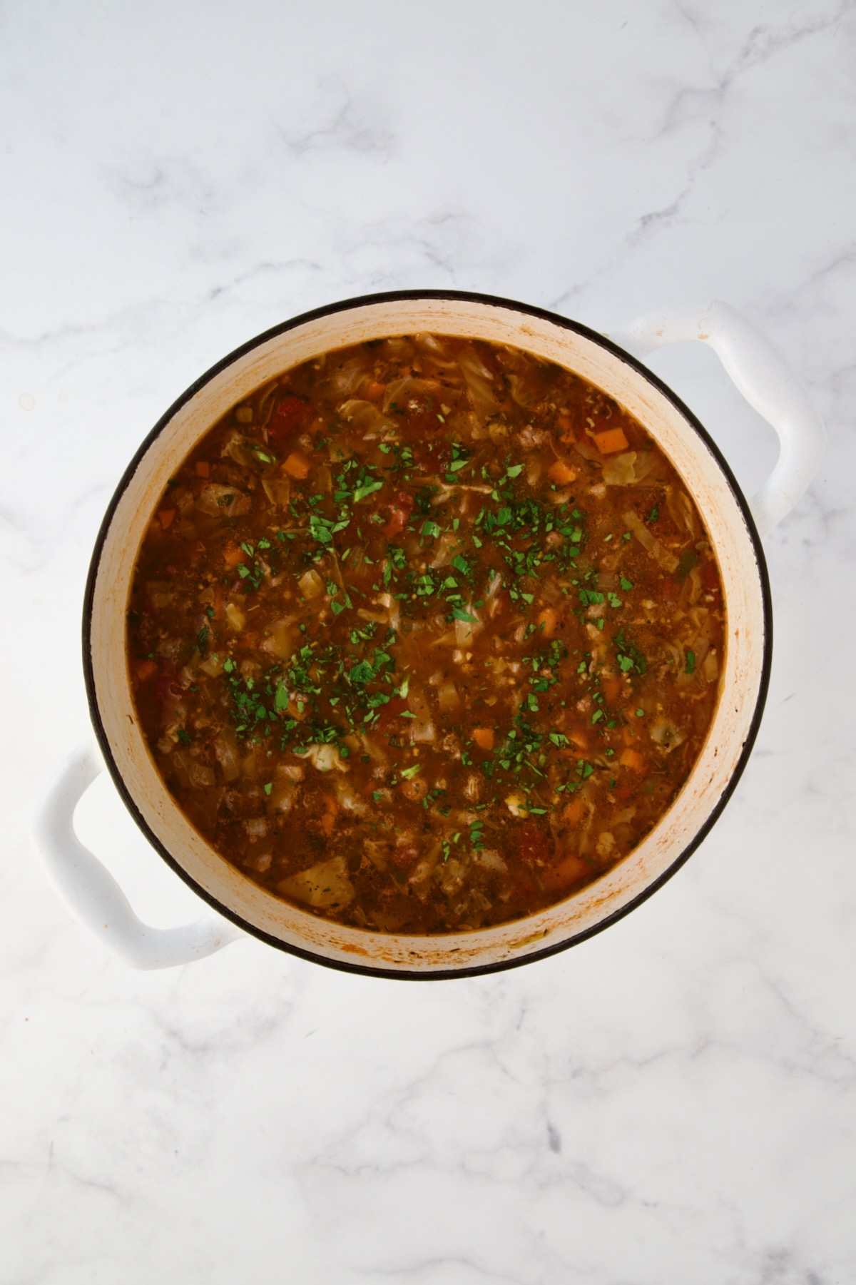 Finished Beef and Cabbage Soup garnished with parsley in white Dutch oven.