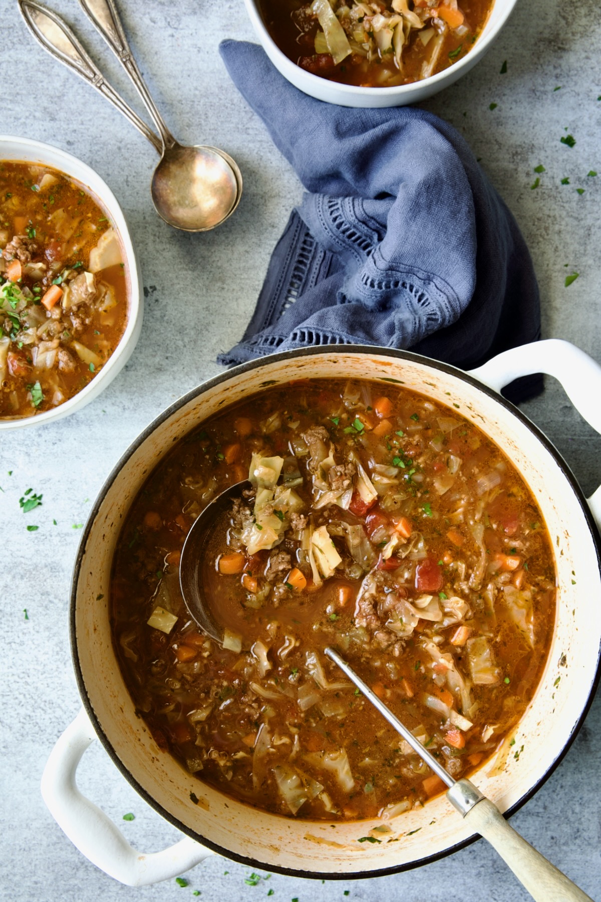 Beef and Cabbage Soup in white Dutch oven with some served into white soup bowls.