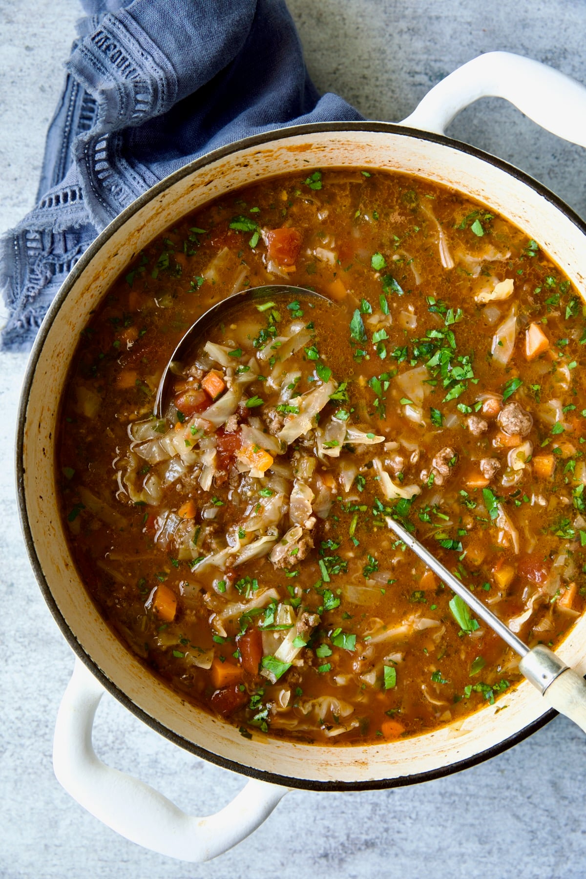 Beef and Cabbage Soup in white Dutch oven with soup ladle.