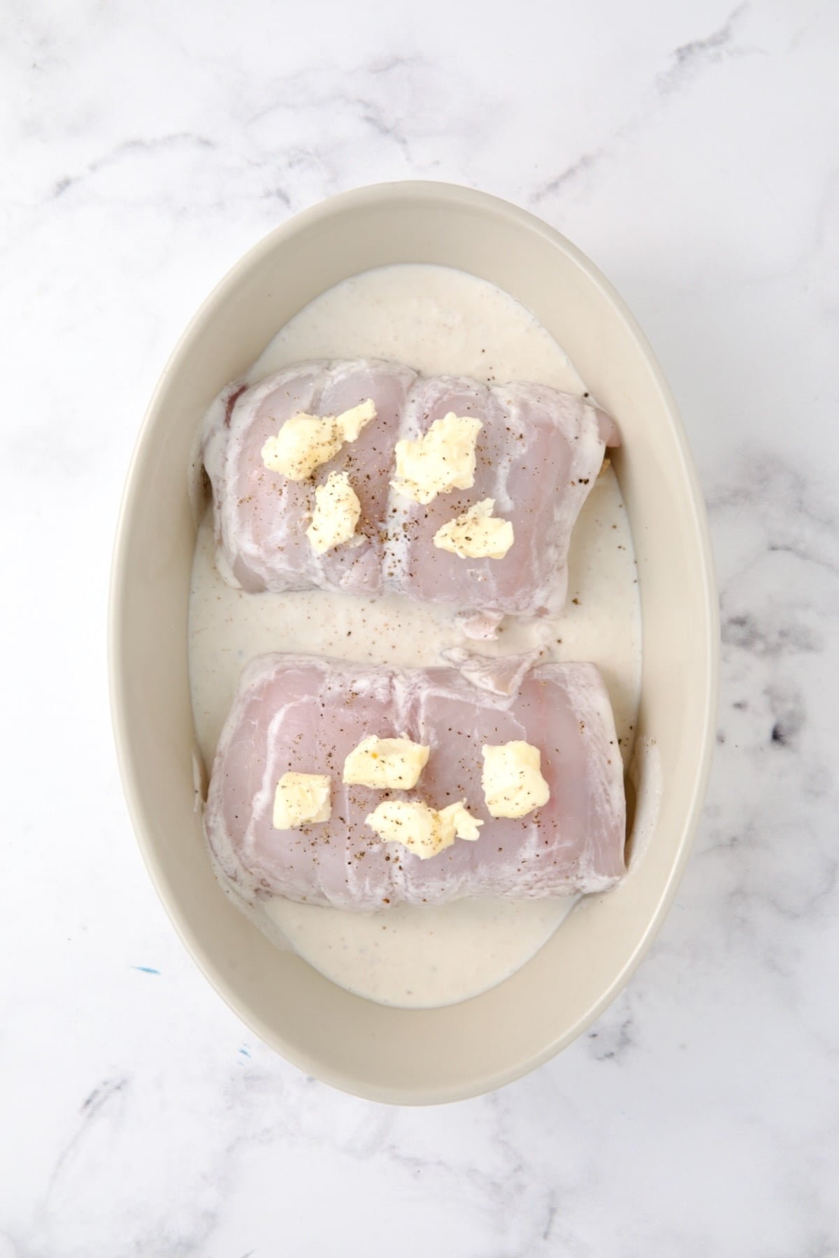 Two uncooked pieces of Crab-Stuffed Flounder in oval baking dish dotted with butter before being baked.
