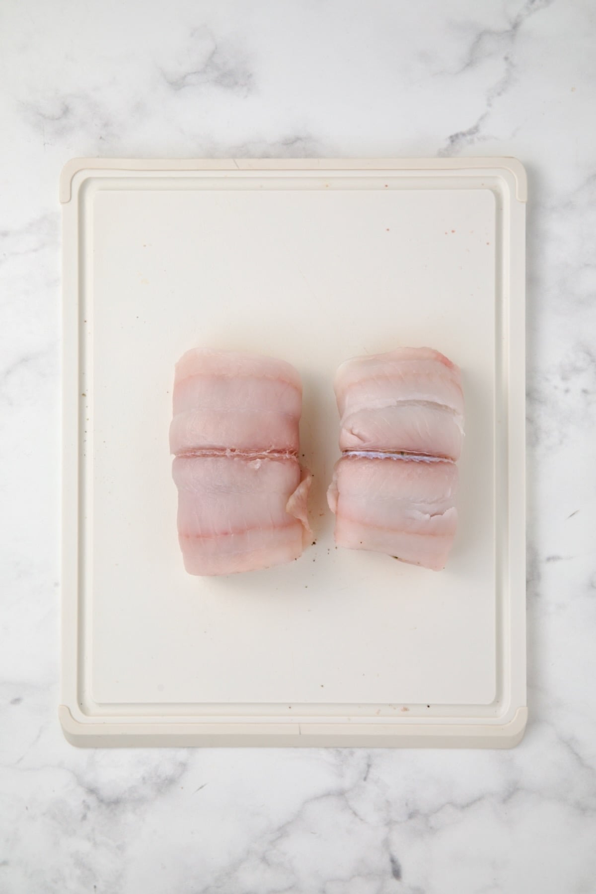 Two flounder fillets on white plastic cutting board rolled to enclose filling.