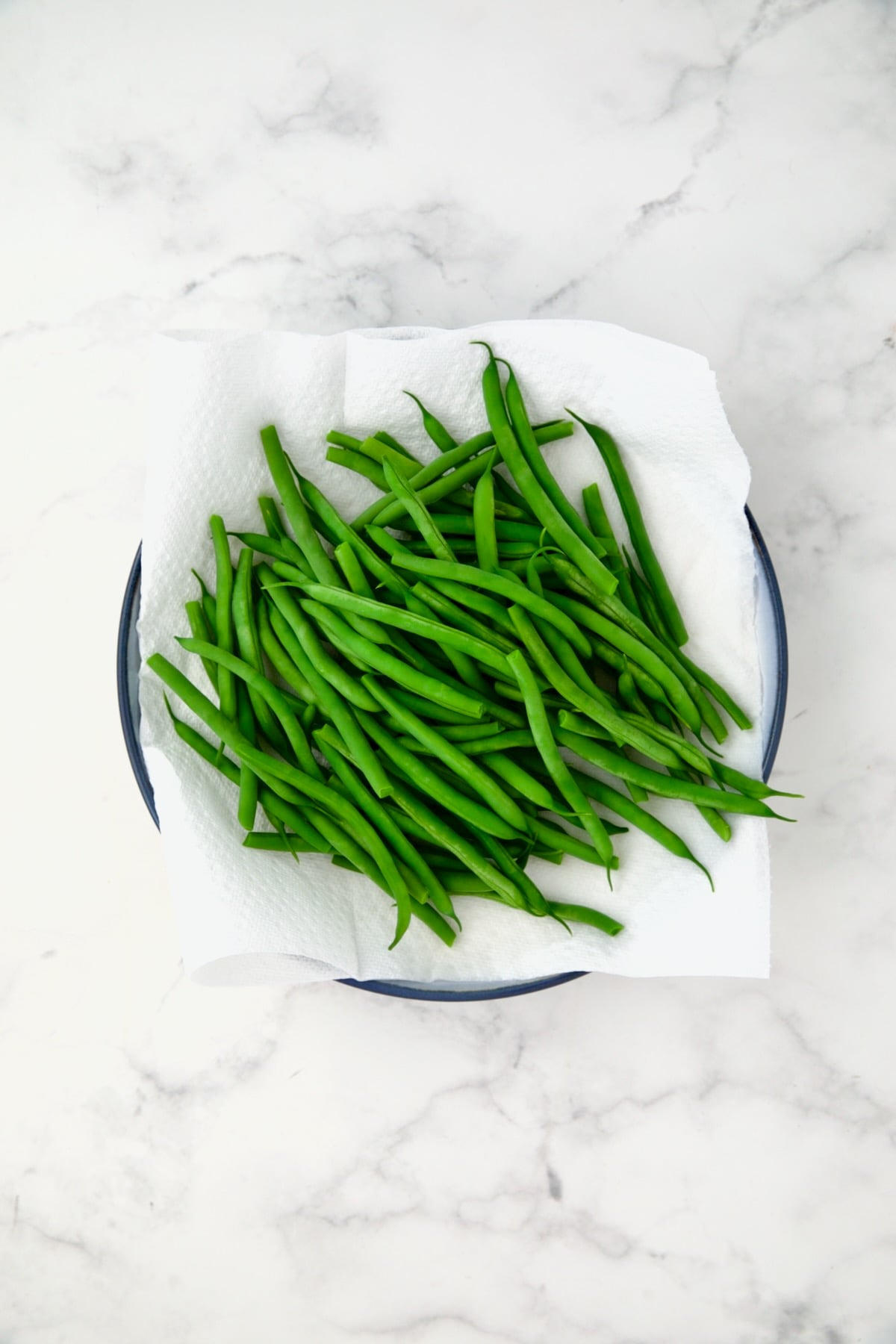 Blanched green beans on paper towel on blue plate.