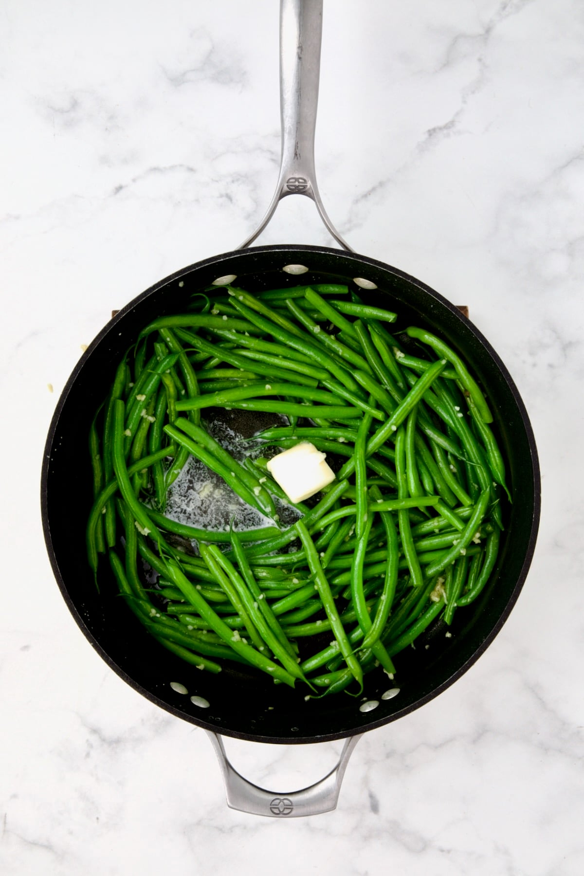 Butter being melted over green beans in nonstick skillet.