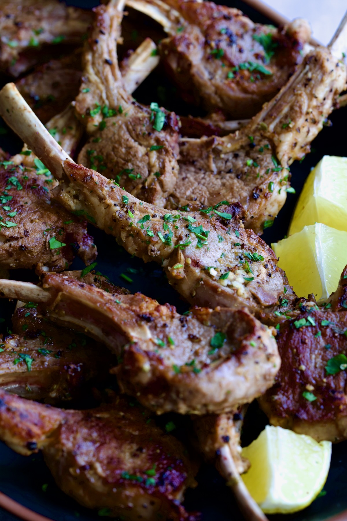 Greek Lamb Chops on black oval platter garnished with lemon wedges.