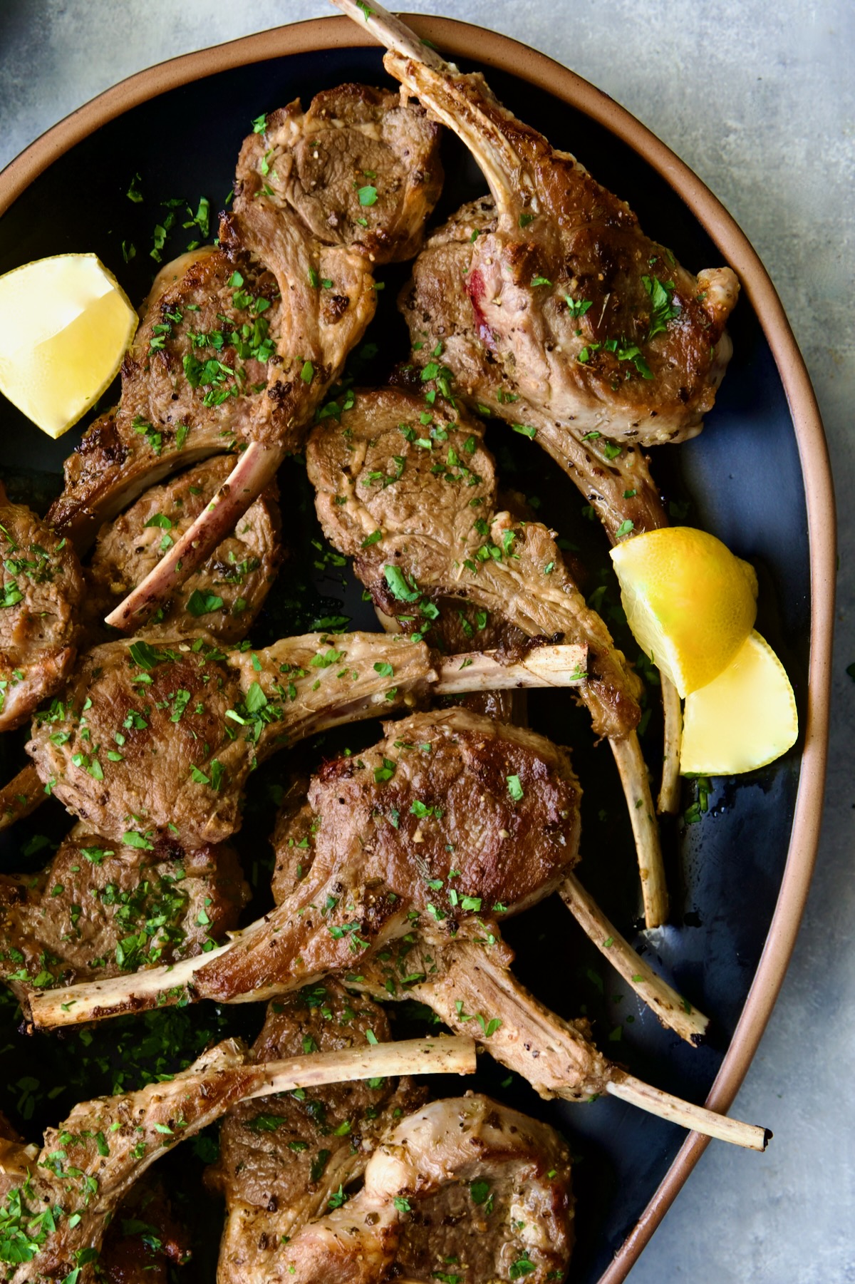 Greek Lamb Chops on black oval platter garnished with lemon wedges.