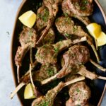 Greek Lamb Chops on black oval platter garnished with lemon wedges.