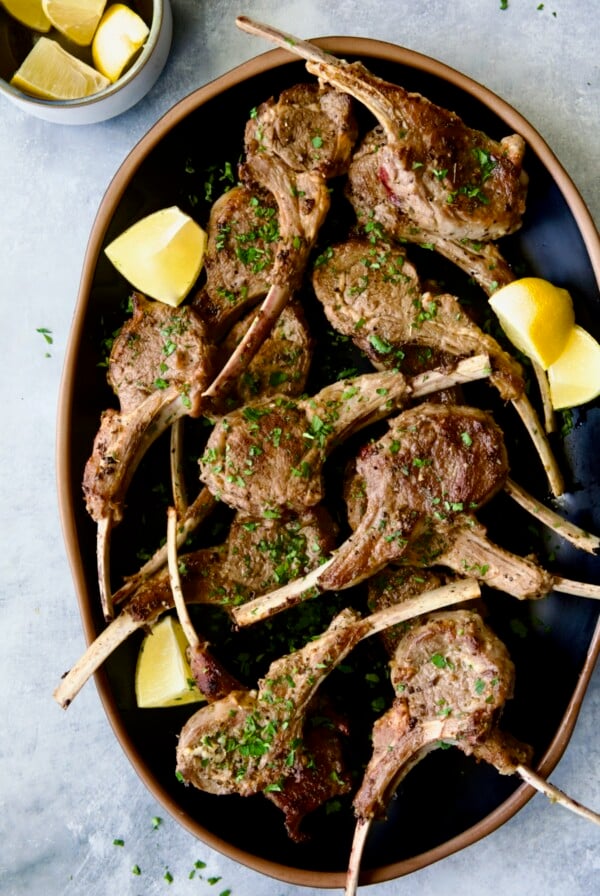 Greek Lamb Chops on black oval platter garnished with lemon wedges.