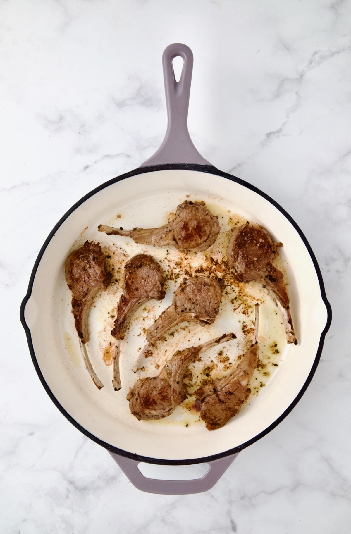 Seven seared lamb chops in white enamel cast iron skillet.