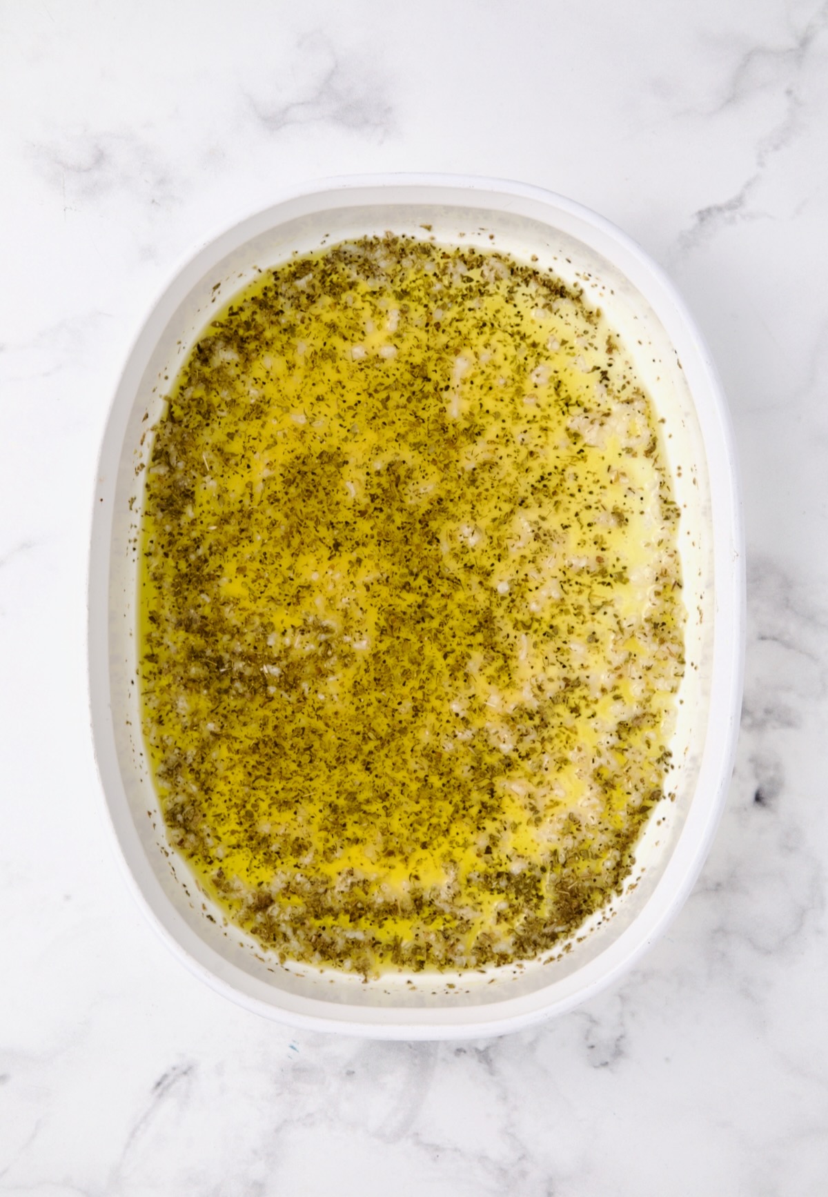 Marinade for lamb chops in oval white baking dish.