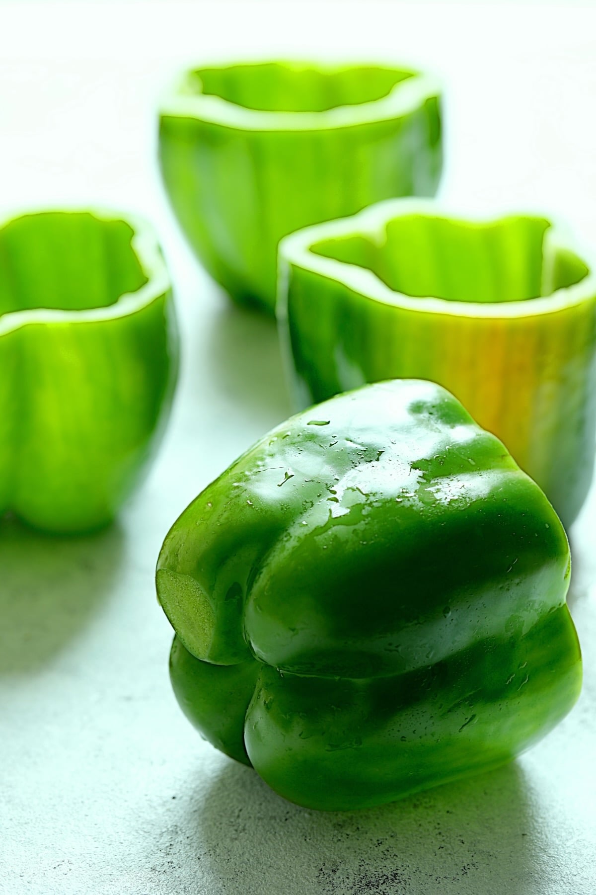 Four green bell peppers with tops removed.