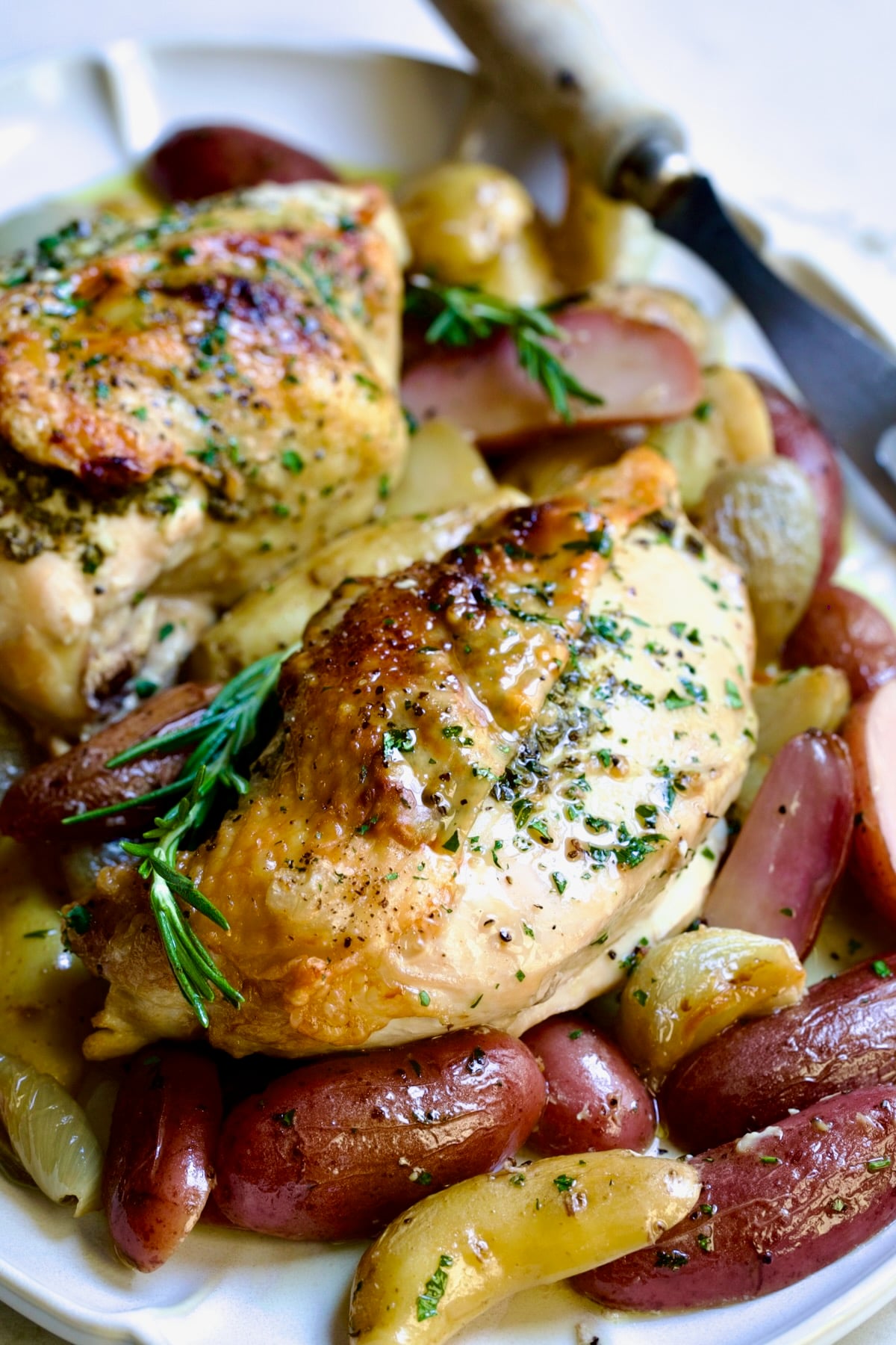 Close-up of Roast Split Chicken Breasts with Potatoes and Shallots on platter with meat fork.