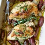 Two Roast Split Chicken Breasts with Potatoes and Shallots in white rectangular baking dish.