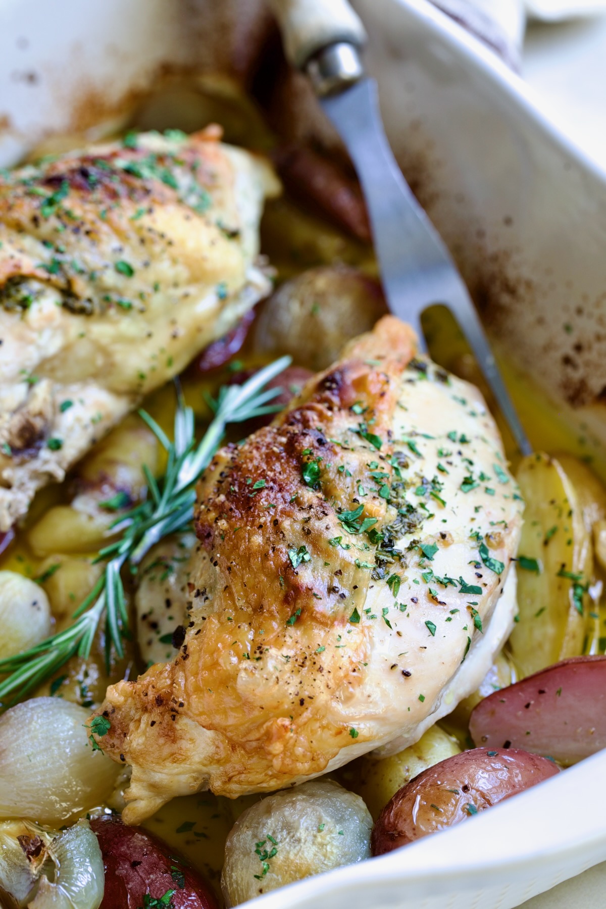 Close-up of Roast Split Chicken Breasts with Potatoes and Shallots on platter with meat fork.