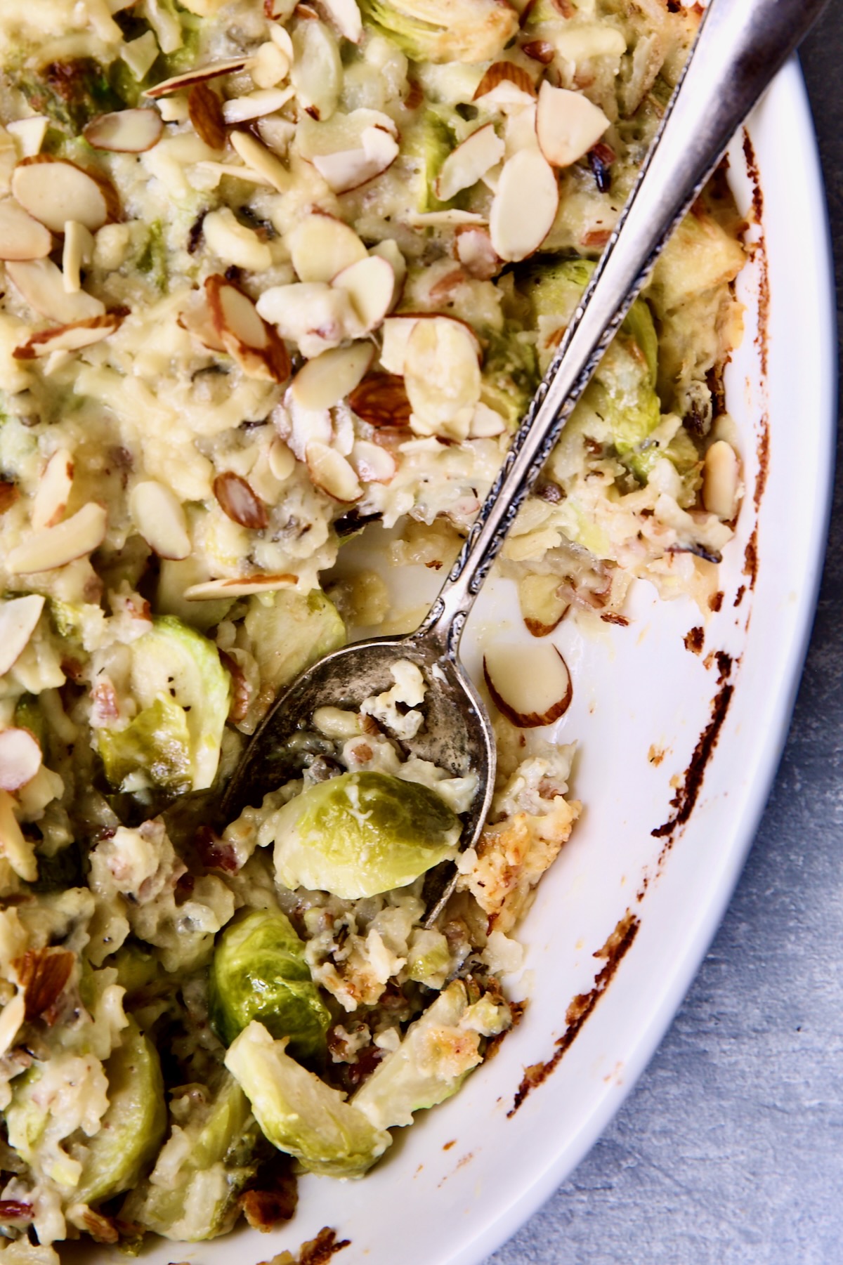Brussels Sprouts Wild Rice Casserole in oval white baking dish with serving spoon scooping some up.