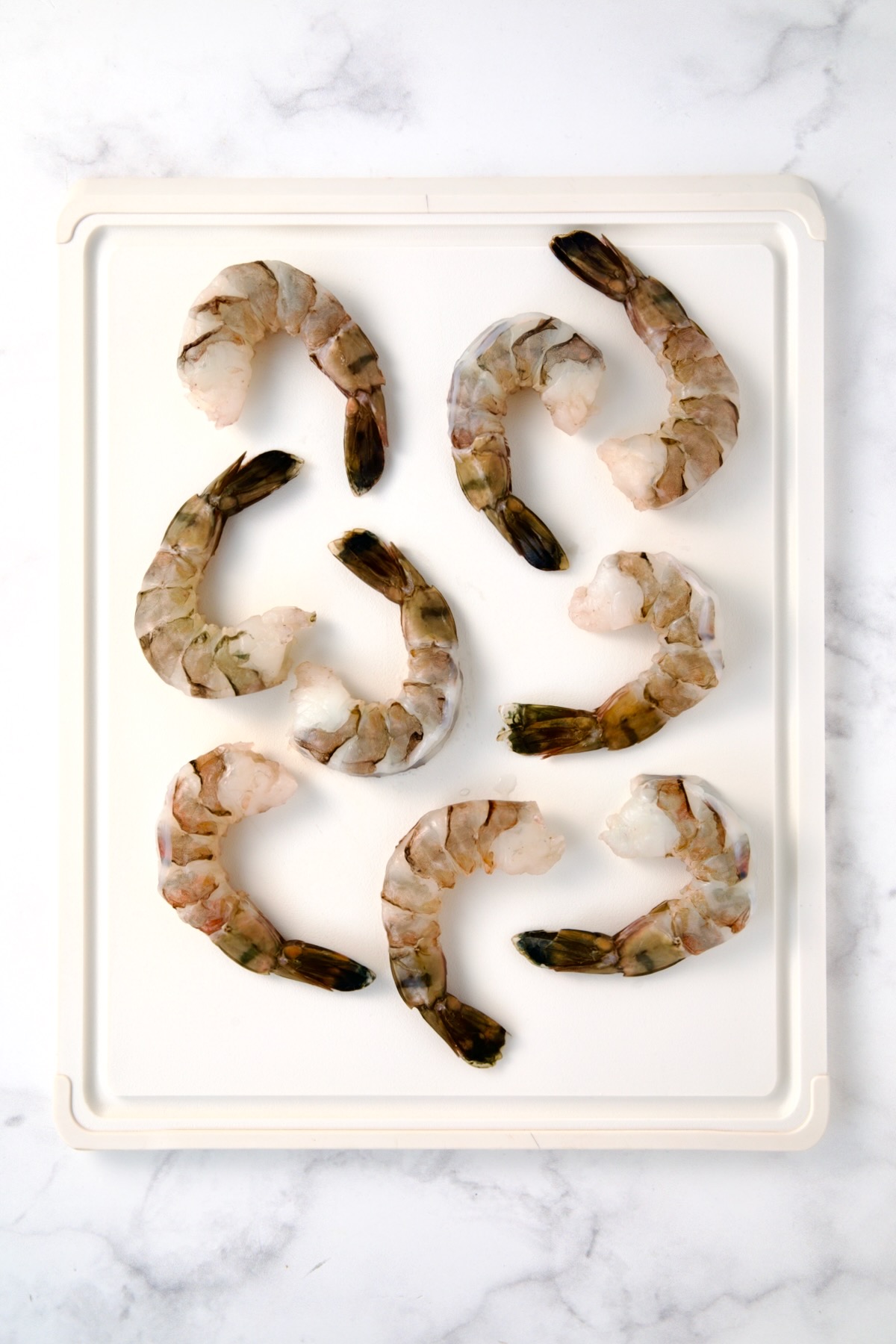 Nine colossal peeled and deveined shrimp on white plastic cutting board.
