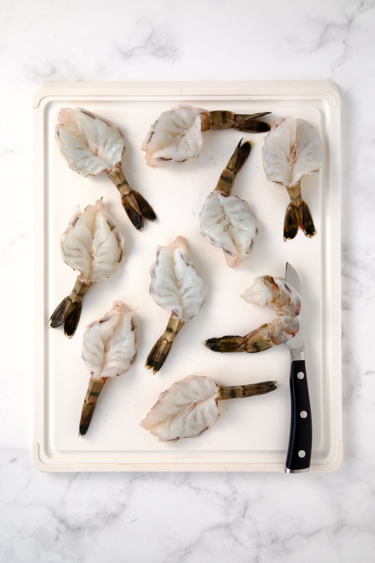 Nine colossal peeled and deveined shrimp on white plastic cutting board after being butterflied.