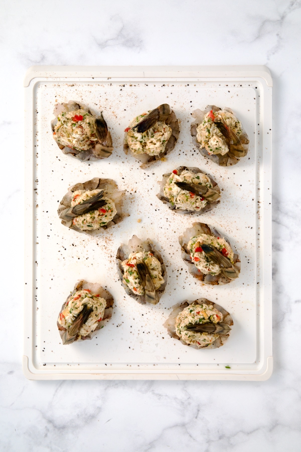 Nine stuffed shrimp on white plastic cutting board after being stuffed with crab filling.
