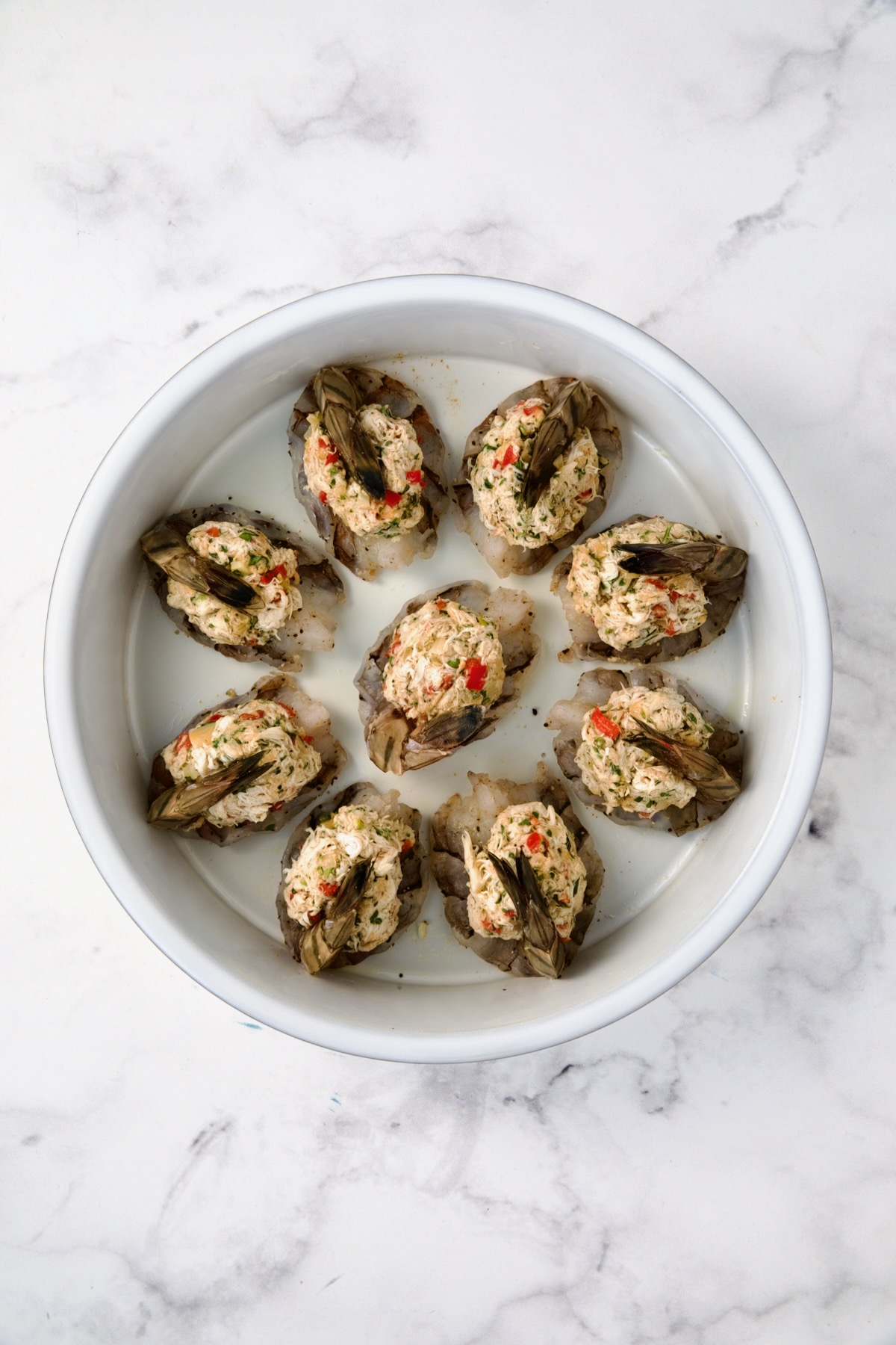 Nine stuffed shrimp in round white baking dish.