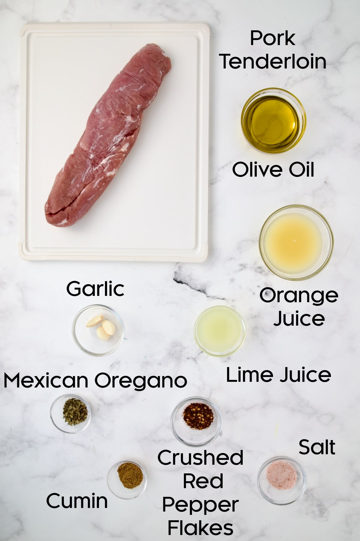 Ingredients for Cuban-Style Pork Tenderloin in glass bowls and uncooked pork tenderloin on white plastic cutting board.
