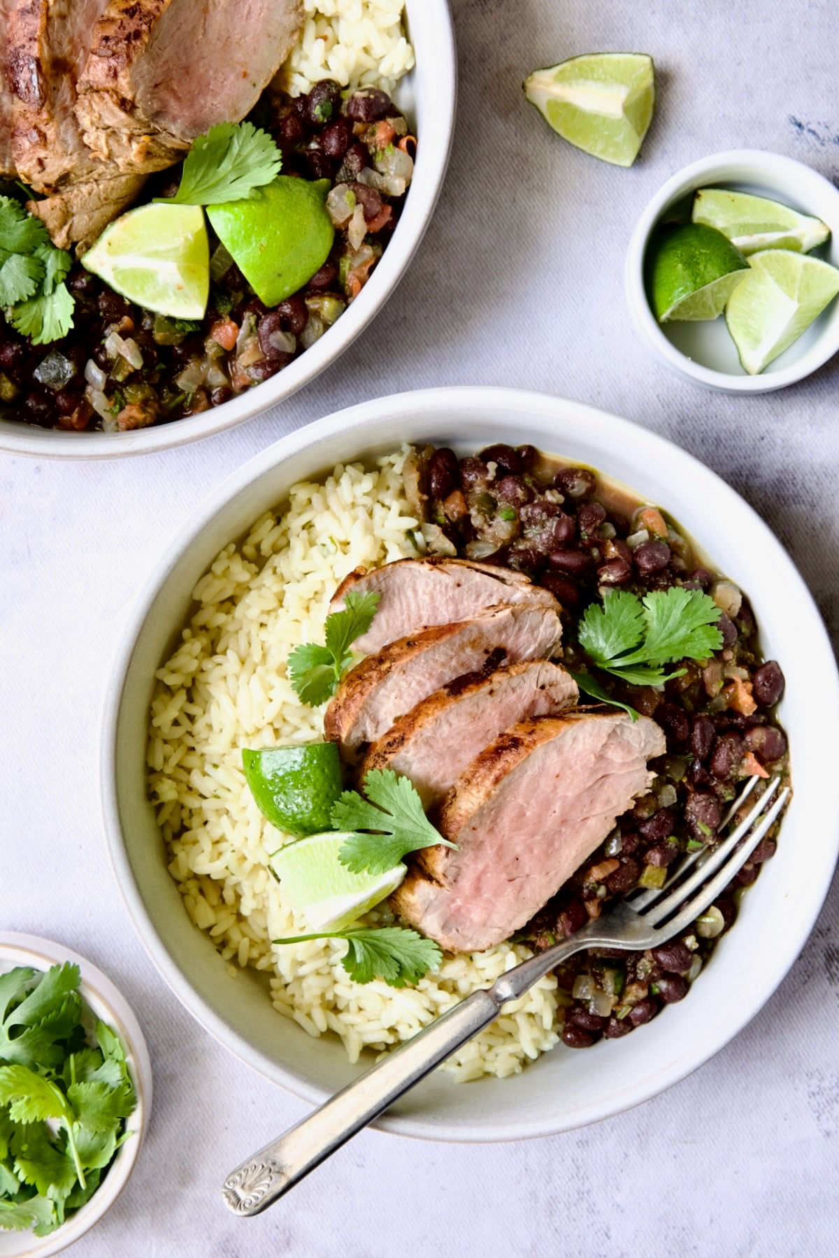 Four slices of Cuban-Style Pork Tenderloin with Black Beans and rice in white bowl.