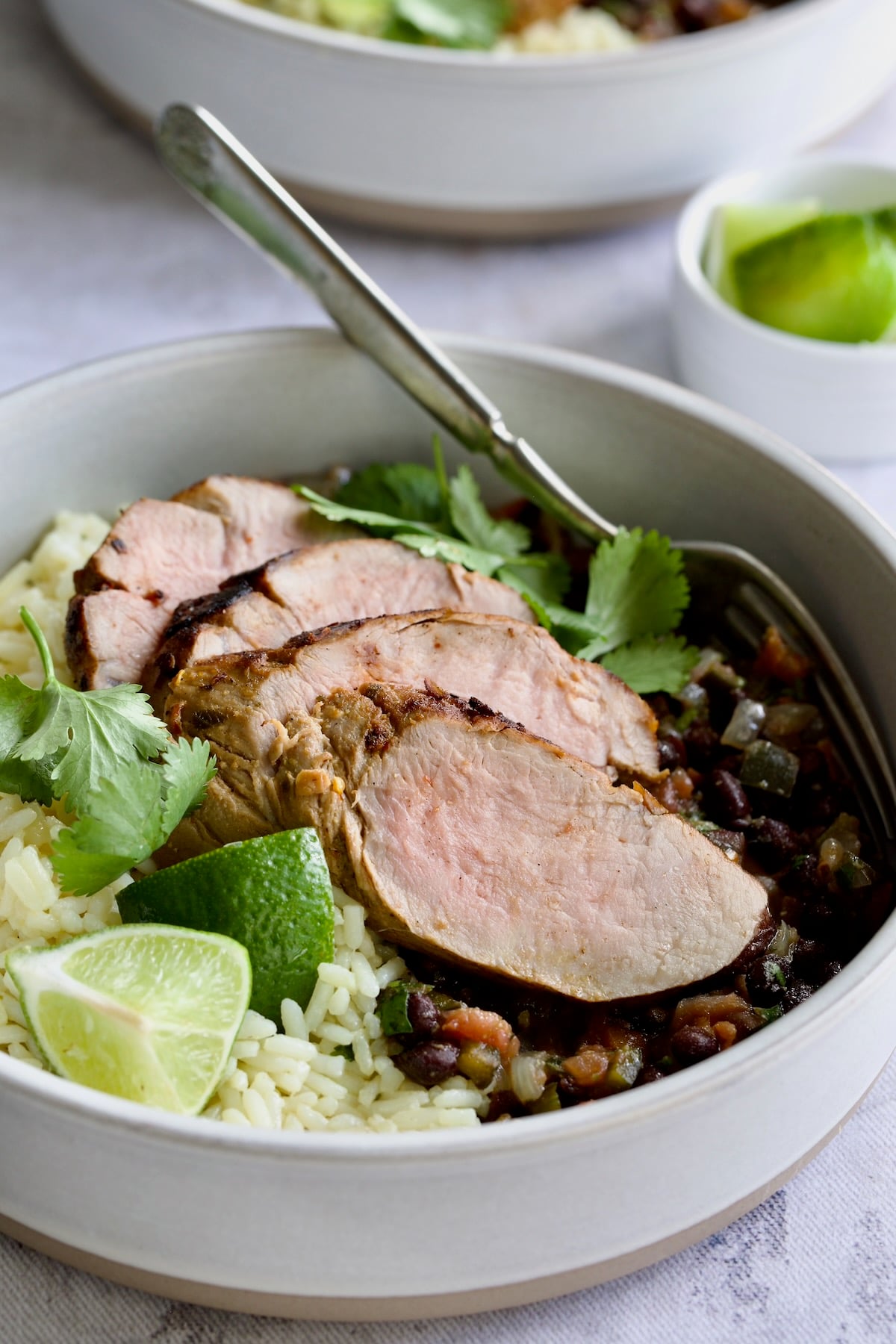 Four slices of Cuban-Style Pork Tenderloin with Black Beans and rice in white bowl.