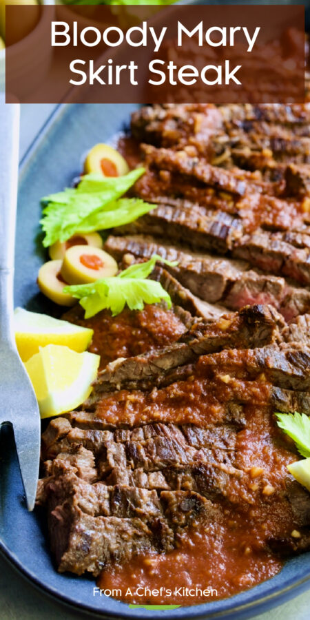 Pinterest graphic for Bloody Mary Skirt Steak showing it on a blue platter garnished with lemon wedges, celery leaves and sliced green olives.