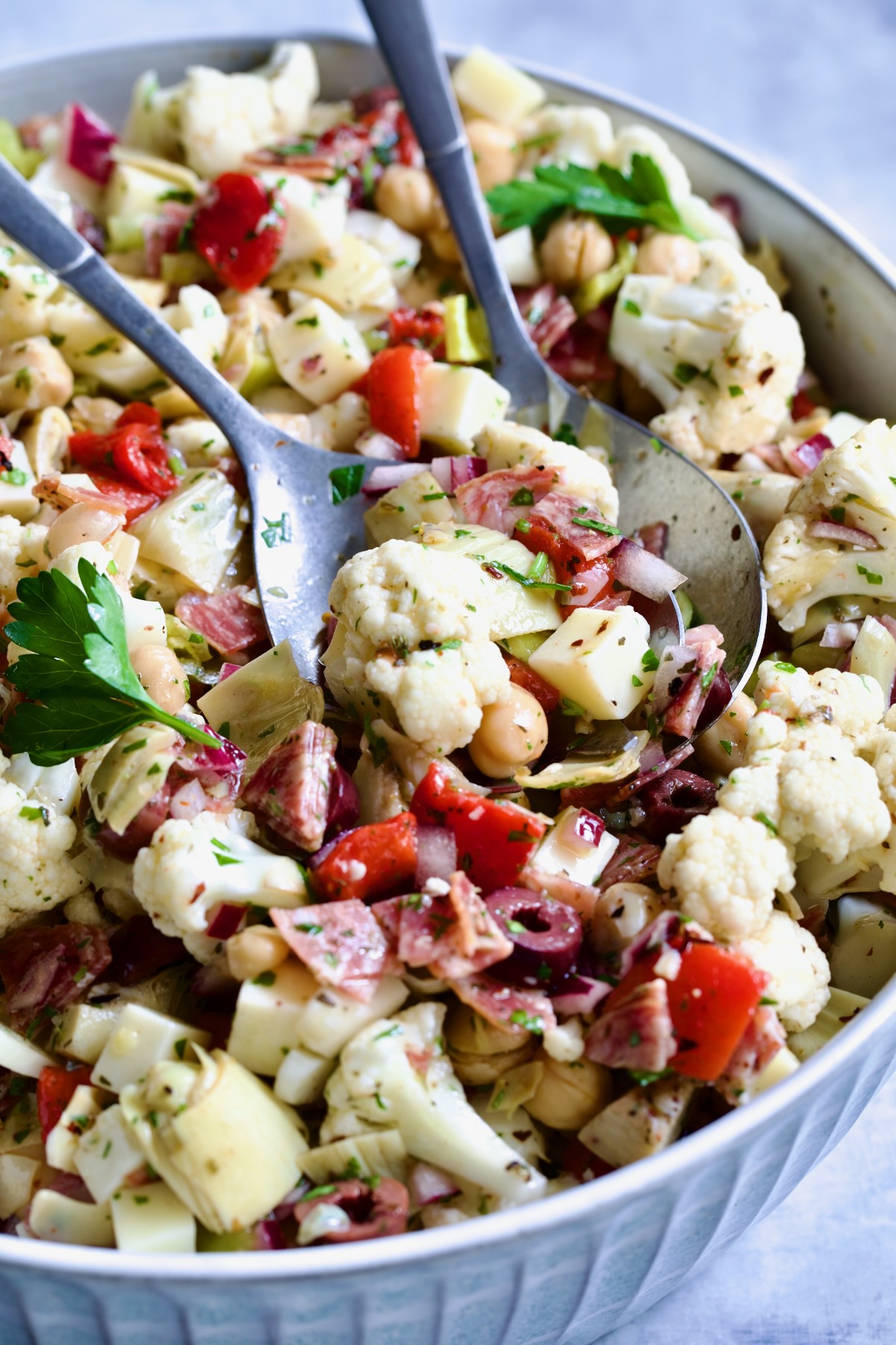 Cauliflower Antipasto Salad in blue serving bowl with serving utensils.