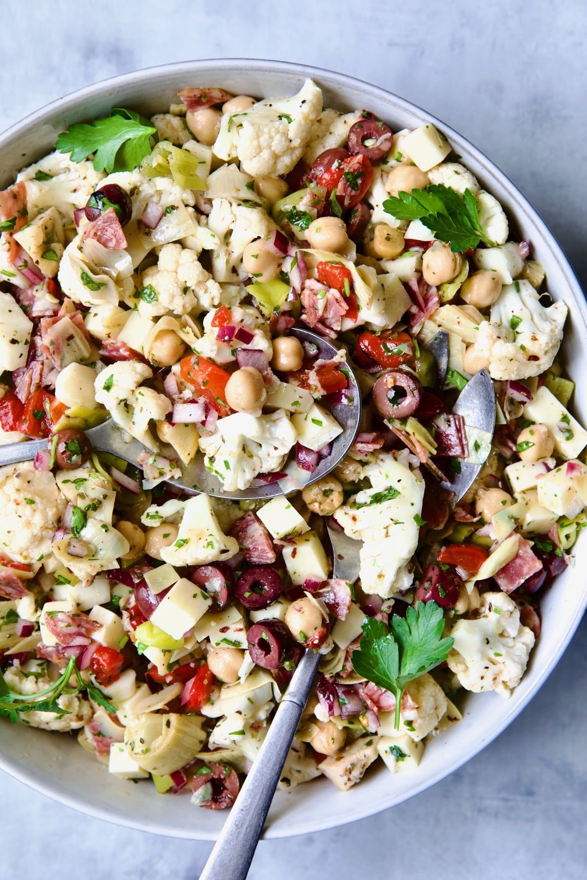 Cauliflower Antipasto Salad in blue serving bowl with serving utensils.