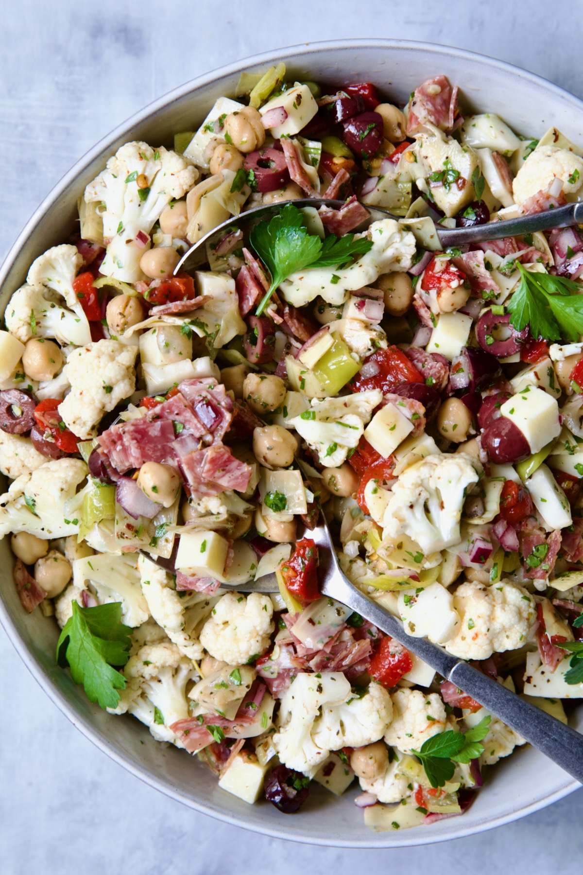Cauliflower Antipasto Salad in serving bowl with serving utensils.