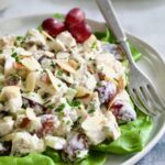 Chicken Salad with Herbs, Almonds and Grapes on lettuce on white plate.
