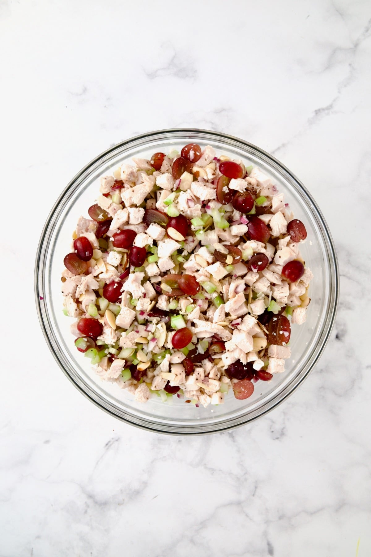Chicken salad ingredients mixed together in glass bowl.