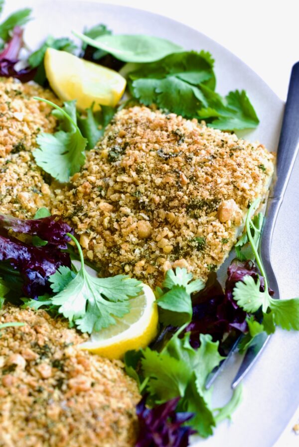 Crispy Chickpea-Crusted Fish on oval white platter garnished with fresh baby greens.